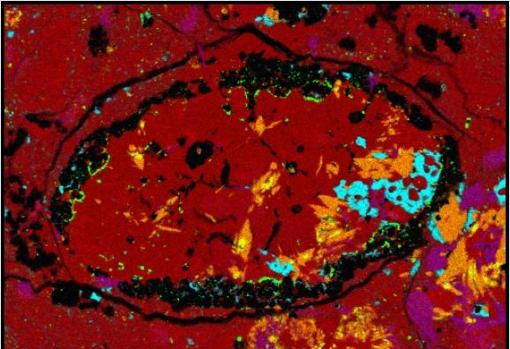 Los científicos de SwRI estudiaron la composición de un pequeño fragmento de un meteoroide para determinar que probablemente se originó a partir de un asteroide padre previamente desconocido. Esta micrografía de color falso de la muestra de meteoroide muestra los cristales anfíbol inesperados identificados en naranja.